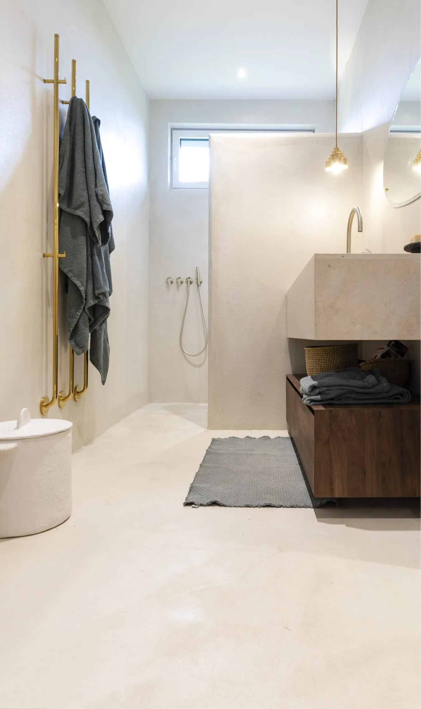 Salle de bain terminée : sol en béton ciré, douche de plain-pied, meuble en noyer et sèche-serviettes laiton