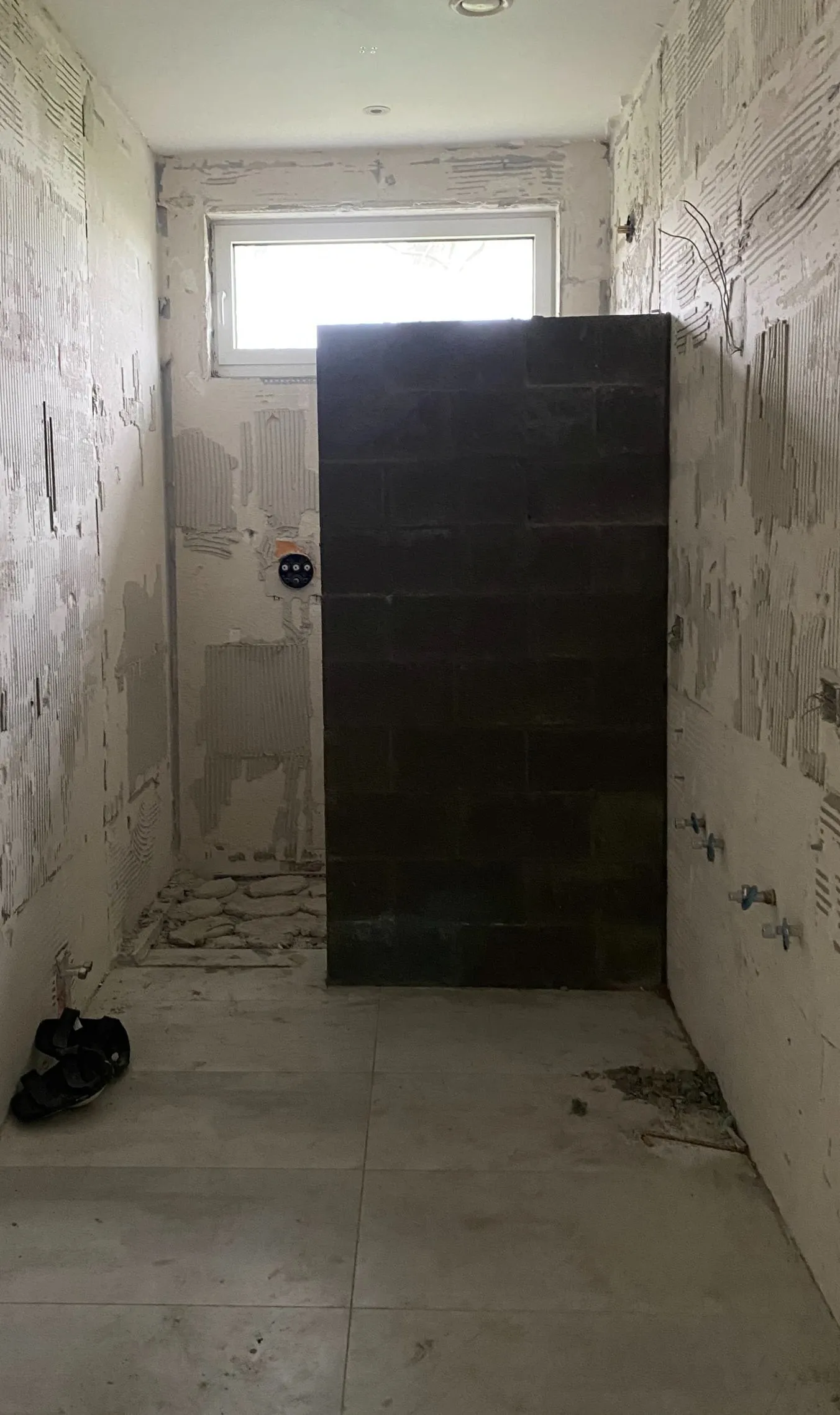Salle de bain mise à nu avant travaux : murs décapés, cloison en blocs, attentes de plomberie apparentes